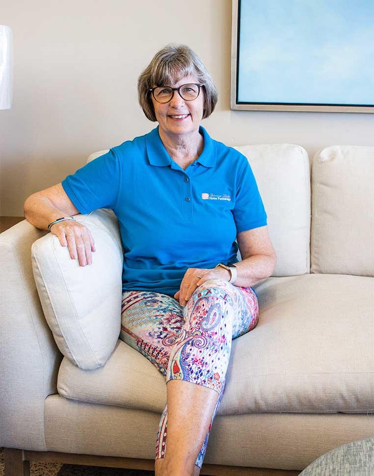 A smiling woman wearing a blue polo shirt sitting on a sofa