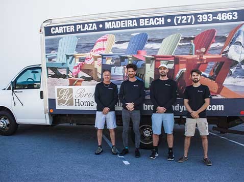 Four men in black shirts standing in a row next to the company truck